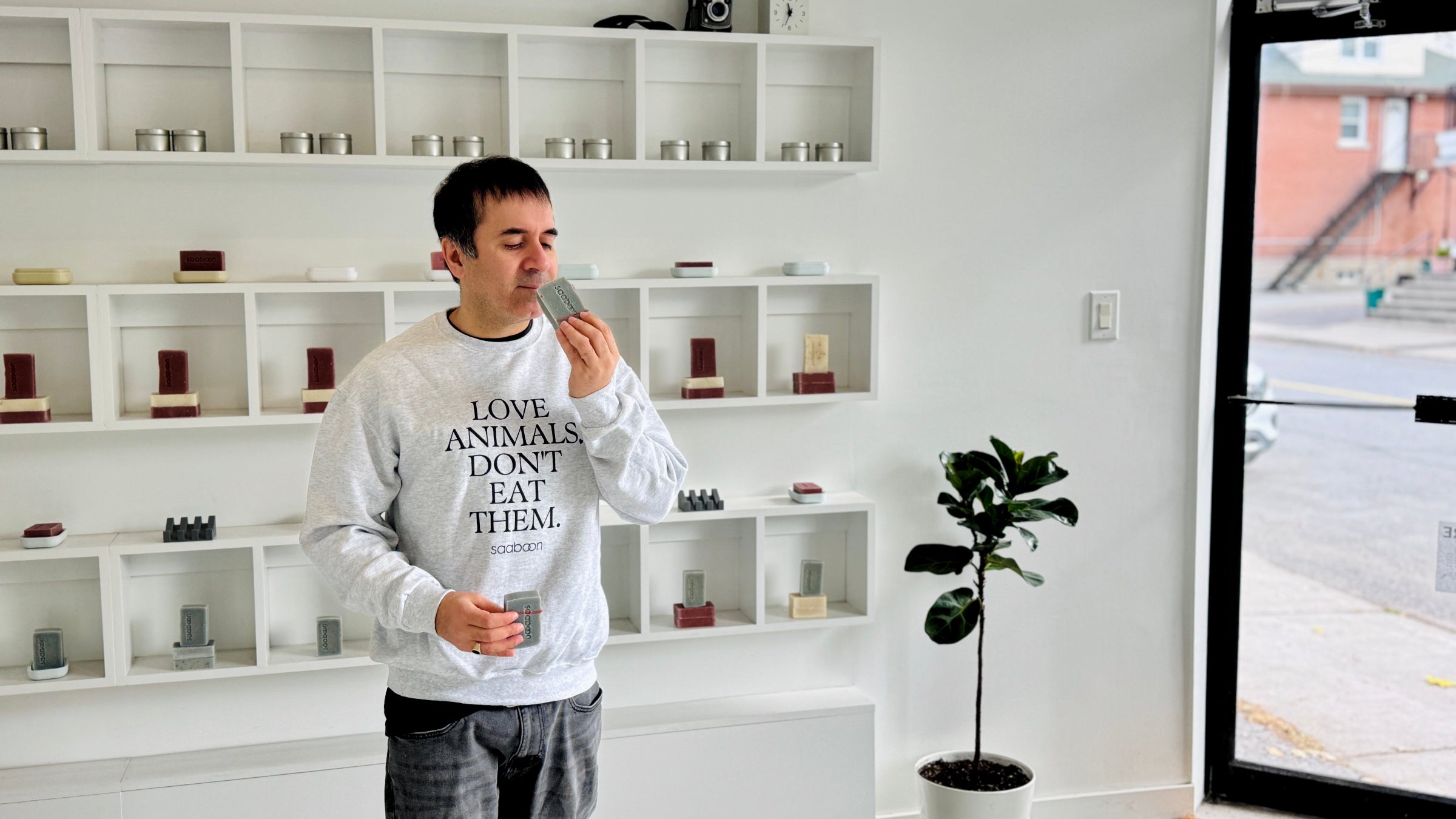 Person wearing a sweatshirt with an animal rights message in a room with shelves and a plant.