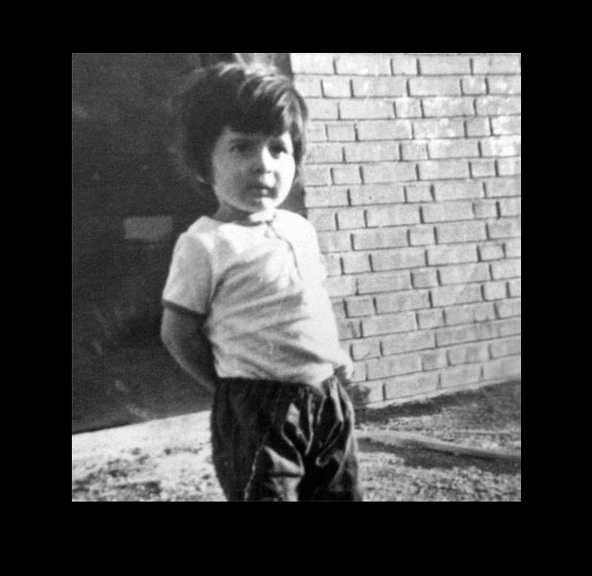 Black and white photo of a child standing in front of a brick wall.